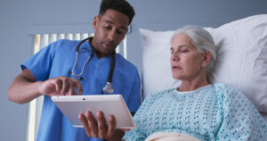Male registered nurse showing ill elderly woman electronic pad